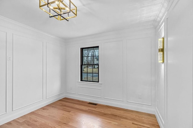 empty room with visible vents, an inviting chandelier, light wood-style flooring, ornamental molding, and a decorative wall