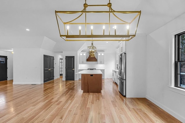 kitchen featuring a center island, white cabinetry, freestanding refrigerator, an inviting chandelier, and light countertops