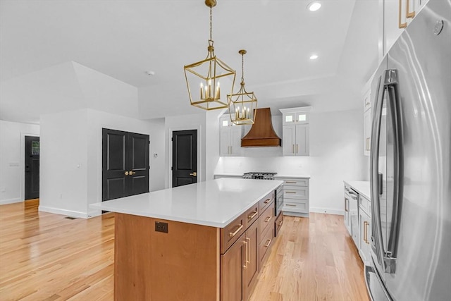 kitchen with a center island, light countertops, freestanding refrigerator, light wood-style floors, and custom exhaust hood