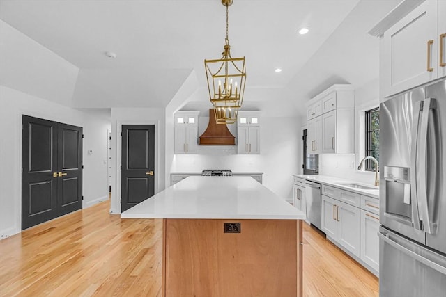 kitchen featuring premium range hood, a sink, a center island, appliances with stainless steel finishes, and white cabinets