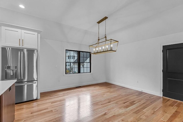 kitchen featuring stainless steel refrigerator with ice dispenser, white cabinetry, light wood-style floors, light countertops, and baseboards