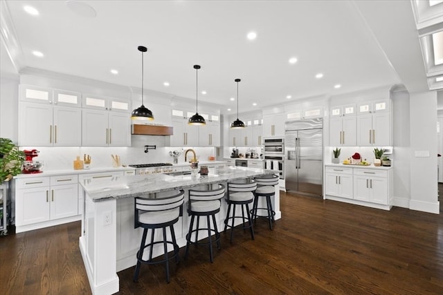 kitchen featuring decorative backsplash, white cabinets, a center island with sink, dark wood-type flooring, and stainless steel appliances