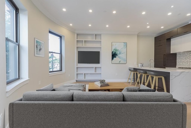 living area featuring built in shelves, recessed lighting, wood finished floors, baseboards, and crown molding