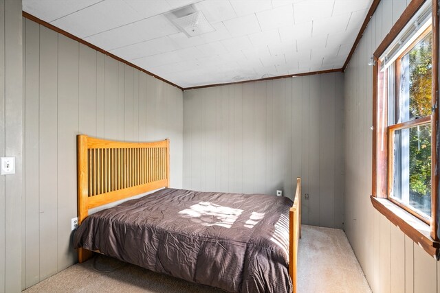 bedroom featuring multiple windows, wooden walls, crown molding, and light carpet