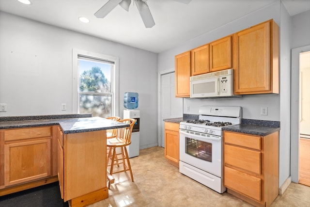 kitchen featuring ceiling fan, a kitchen bar, white appliances, and kitchen peninsula