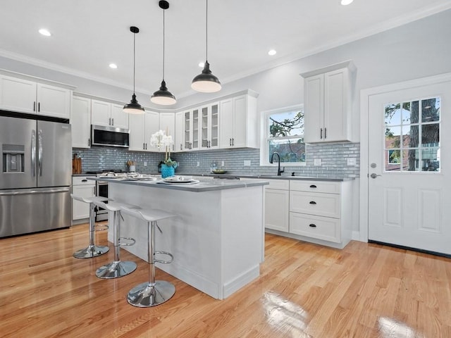 kitchen with appliances with stainless steel finishes, a breakfast bar, white cabinetry, hanging light fixtures, and a center island