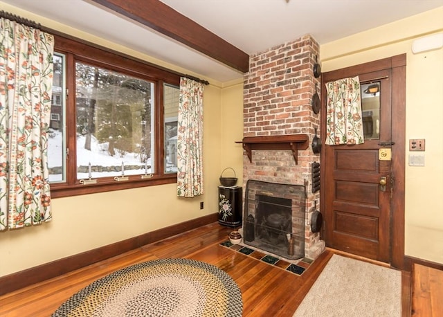 living area with baseboards, beamed ceiling, wood finished floors, and a brick fireplace