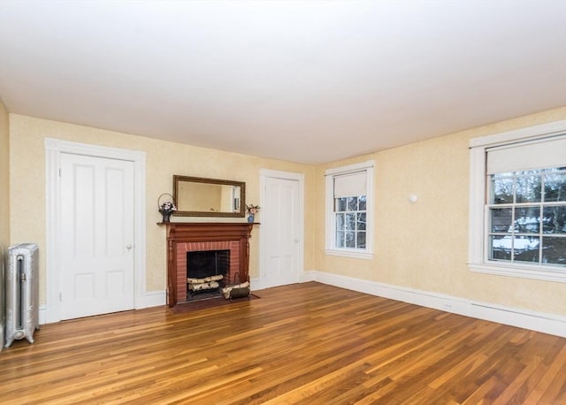 unfurnished living room featuring baseboards, wood finished floors, radiator heating unit, and a brick fireplace