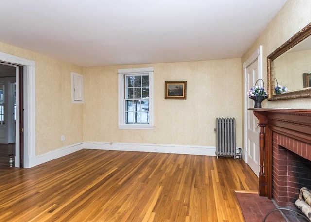 unfurnished living room with baseboards, wood finished floors, radiator heating unit, and a brick fireplace