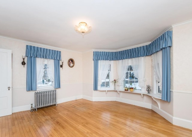empty room featuring radiator, light wood-style floors, baseboards, and ornamental molding