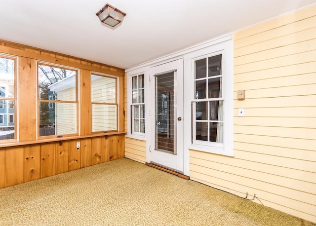 unfurnished sunroom with carpet flooring and wood walls