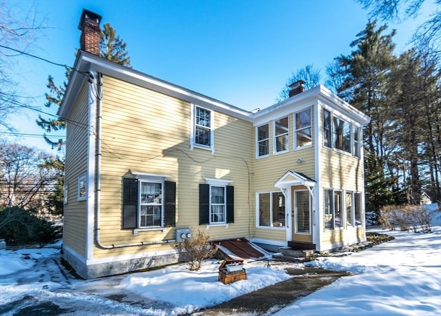 snow covered rear of property with a chimney