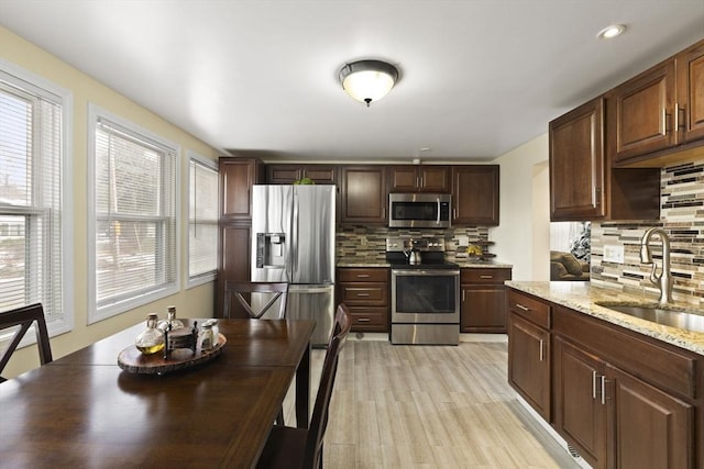 kitchen featuring light stone countertops, appliances with stainless steel finishes, backsplash, sink, and light hardwood / wood-style floors