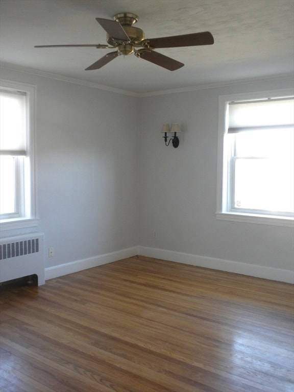 empty room with dark hardwood / wood-style flooring, radiator, a healthy amount of sunlight, and ceiling fan