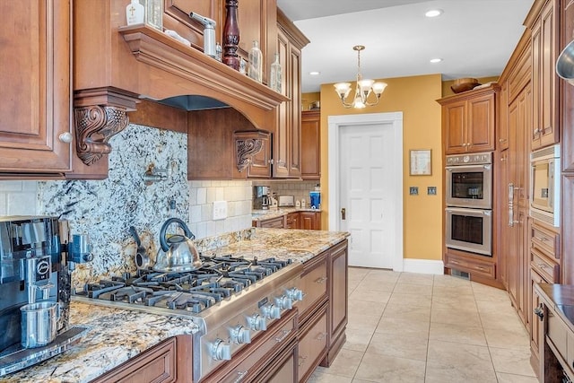 kitchen with light tile patterned floors, appliances with stainless steel finishes, an inviting chandelier, backsplash, and light stone counters