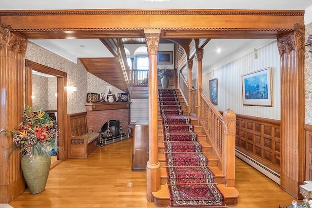 stairs featuring hardwood / wood-style floors, a baseboard radiator, decorative columns, and a fireplace