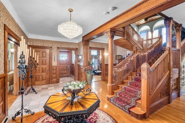 foyer with crown molding, a chandelier, light hardwood / wood-style floors, and ornate columns