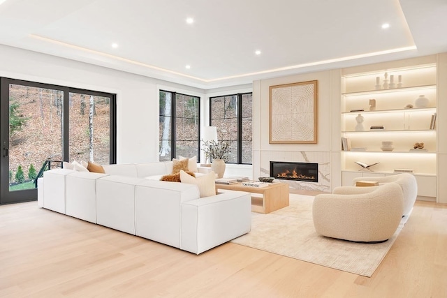 living room featuring light wood-type flooring, a tray ceiling, and a high end fireplace