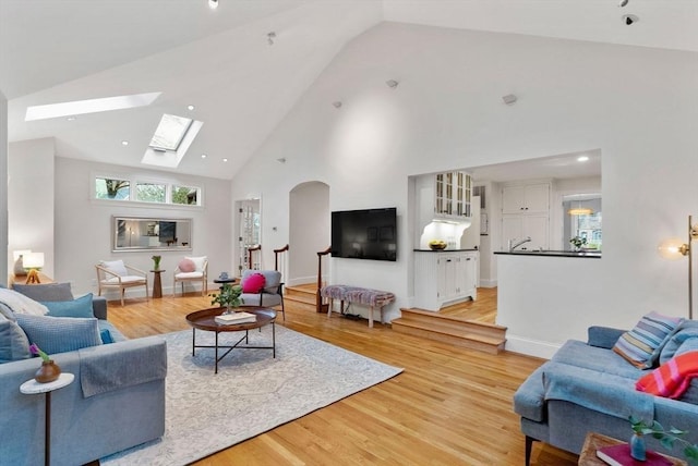 living area with arched walkways, baseboards, high vaulted ceiling, and light wood-style floors