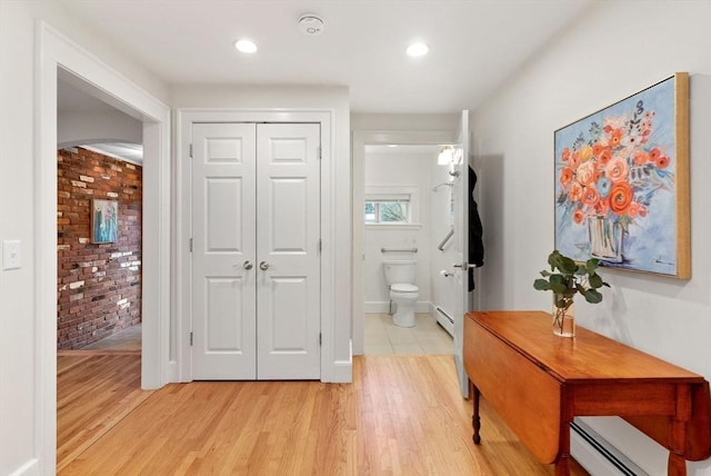 bathroom featuring toilet, wood finished floors, brick wall, and a baseboard radiator