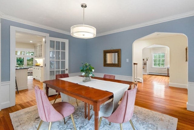 dining space featuring a baseboard heating unit, arched walkways, light wood-style floors, and crown molding