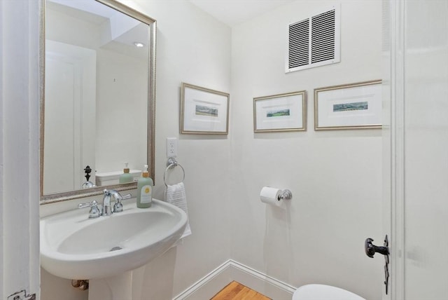 half bath featuring wood finished floors, baseboards, visible vents, a sink, and toilet