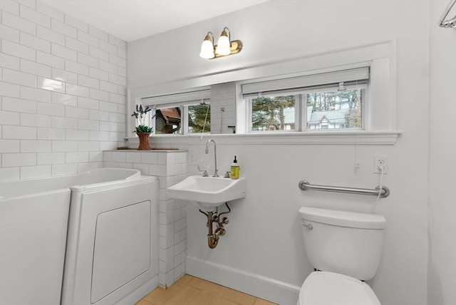 bathroom with a bath, baseboards, washer / dryer, a sink, and toilet