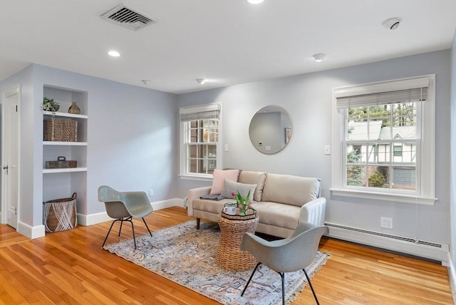 living area with built in features, wood finished floors, visible vents, baseboards, and a baseboard heating unit