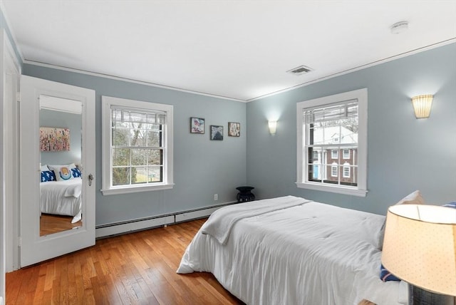 bedroom featuring visible vents, ornamental molding, a baseboard heating unit, and hardwood / wood-style flooring