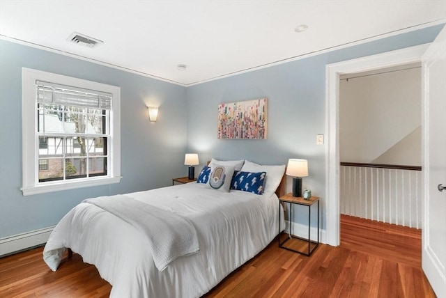 bedroom featuring visible vents, ornamental molding, a baseboard heating unit, wood finished floors, and baseboards