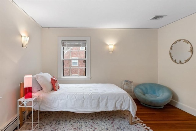 bedroom with a baseboard heating unit, wood finished floors, visible vents, and baseboards