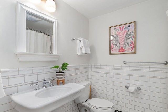 bathroom featuring a wainscoted wall, toilet, tile walls, and a sink