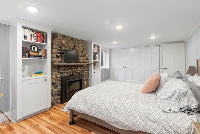 bedroom featuring a stone fireplace, two closets, recessed lighting, and light wood finished floors