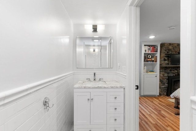 bathroom featuring a wainscoted wall, vanity, a stone fireplace, wood finished floors, and tile walls