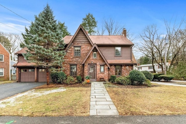 english style home with brick siding, aphalt driveway, a front yard, a chimney, and a garage