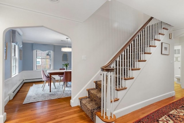 staircase featuring baseboards, arched walkways, wood finished floors, and crown molding