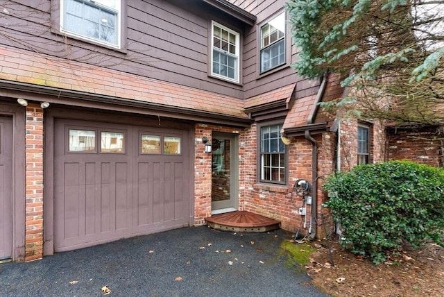 view of exterior entry with aphalt driveway, brick siding, and an attached garage