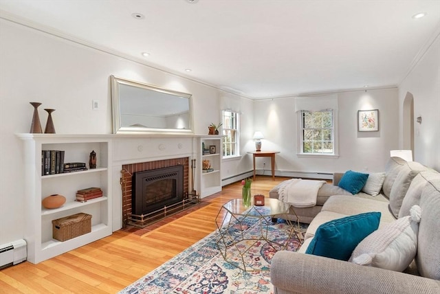 living room with a brick fireplace, ornamental molding, baseboard heating, wood finished floors, and arched walkways