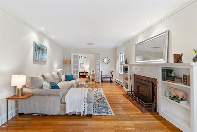 living room with visible vents, ornamental molding, baseboard heating, light wood-style flooring, and a fireplace