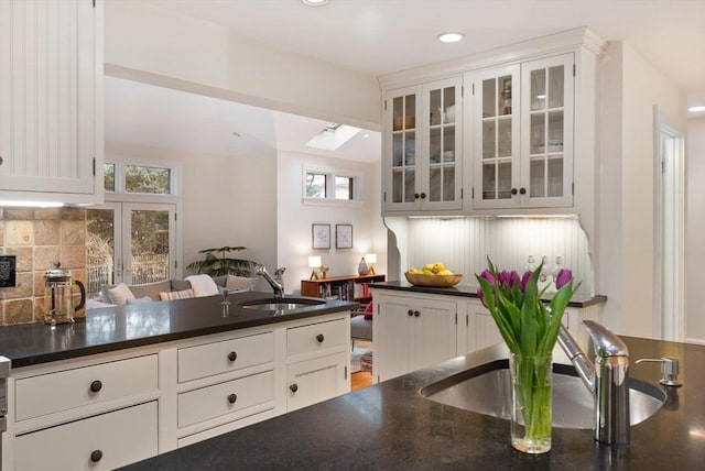 kitchen featuring decorative backsplash, dark countertops, white cabinets, and a sink