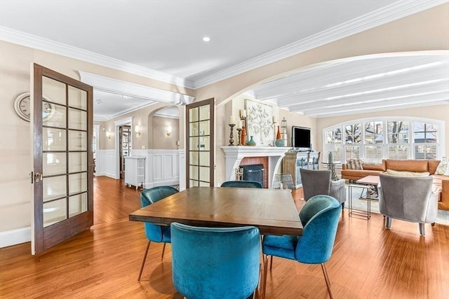 dining space with arched walkways, french doors, a fireplace, and wood finished floors