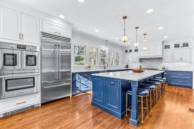 kitchen featuring blue cabinetry, light countertops, appliances with stainless steel finishes, glass insert cabinets, and white cabinetry