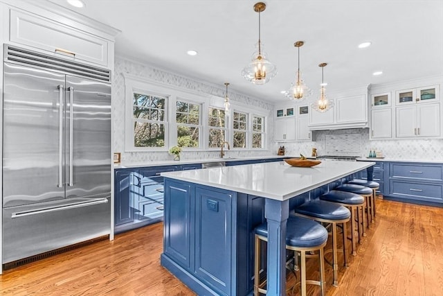 kitchen with blue cabinets, glass insert cabinets, light countertops, and built in fridge