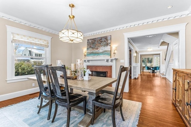 dining room featuring ornamental molding, stairway, a brick fireplace, and wood finished floors