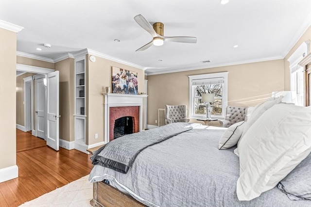 bedroom featuring a brick fireplace, crown molding, multiple windows, and wood finished floors