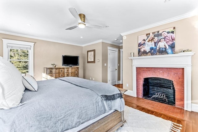 bedroom with ceiling fan, wood finished floors, baseboards, a brick fireplace, and crown molding