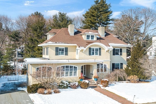 view of front of home with roof with shingles, a chimney, a porch, and stucco siding