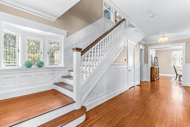 staircase with crown molding, a decorative wall, and wood finished floors