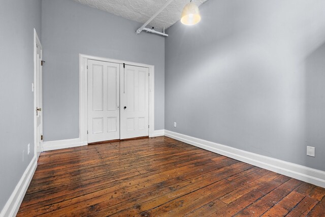 unfurnished bedroom with a towering ceiling, dark hardwood / wood-style flooring, a textured ceiling, and a closet