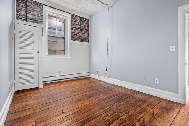 spare room with dark wood-type flooring, a baseboard radiator, and brick wall